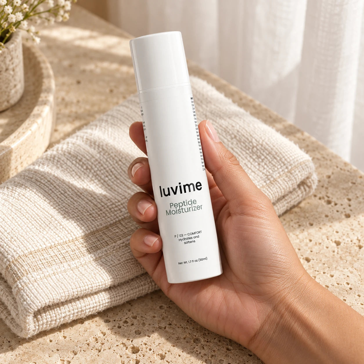 Luvime Peptide Moisturizer cradled in a hand above ivory linen and travertine